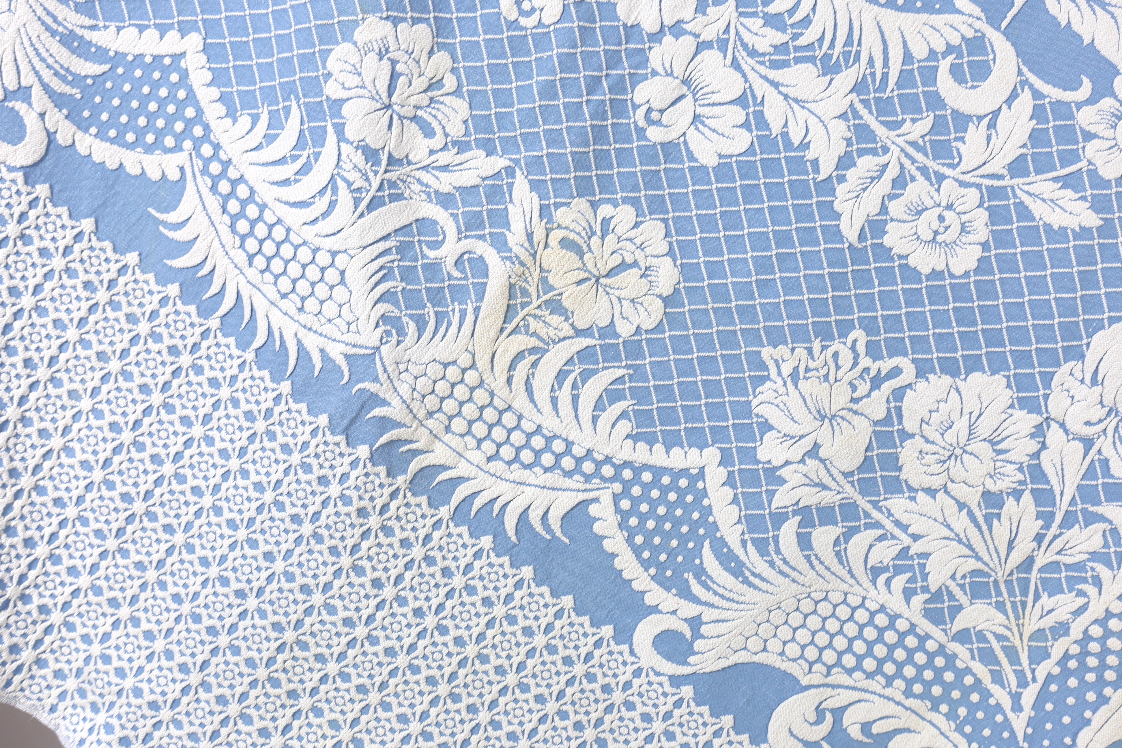 An early 20th century woven 'Marcella' style bed cover, with a blue ground and a white raised floral central cartouche and a wide patterned border, bed cover 194cm wide x 225cm long